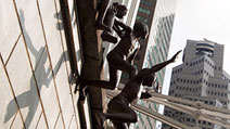 Photograph of bronze sculptures, The First Generation by Chong Fah Cheong, showing five boys jumping happily into the Singapore River, a common scene in the old days, with the Cavenagh Bridge and tall modern buildings as the backdrop, at Boat Quay, Singapore.